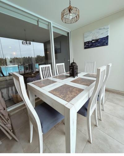 a white dining room table with white chairs and a chandelier at Depto Frente a Laguna y Patio Privado in San Antonio