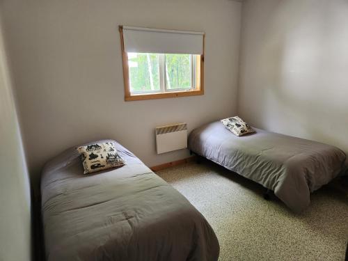 deux lits dans une petite pièce avec une fenêtre dans l'établissement Chalet au lac Saint-Jean, à Dolbeau-Mistassini