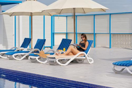 a woman sitting in lounge chairs next to a swimming pool at JA The Manor Hotel, Dubai in Dubai