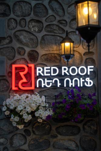a red roof sign on a stone wall with lights and flowers at REDROOF country house hotel in Goris