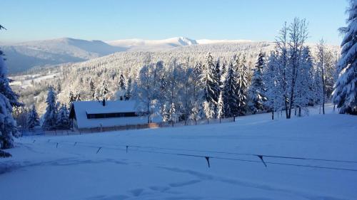a house in the snow with trees and mountains at Penzion Na Začátku in Benecko