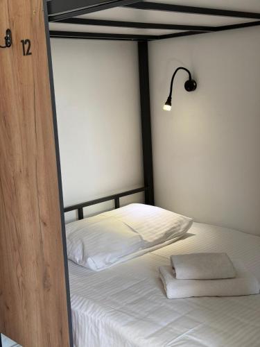a bed with white sheets and a lamp on it at Kerege Guesthouse & Hostel in Bishkek