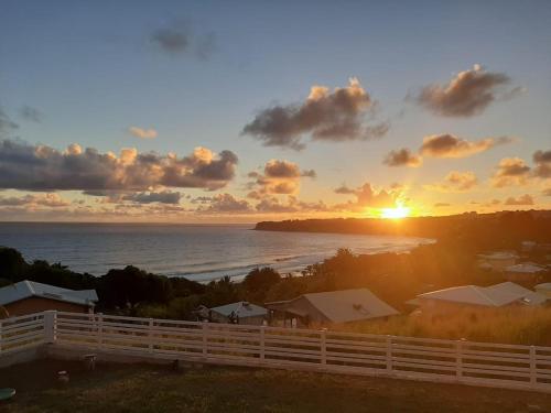 a sunset over the ocean with a white fence at Les Tourterelles - Appartement vue mer & jacuzzi in Le Lorrain