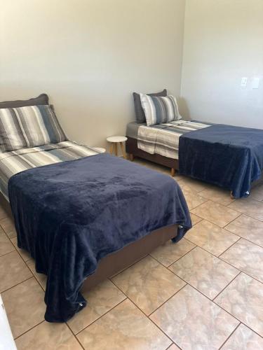 two beds with blue covers in a room with a tile floor at Chalés no Quintal in Alvorada do Sul