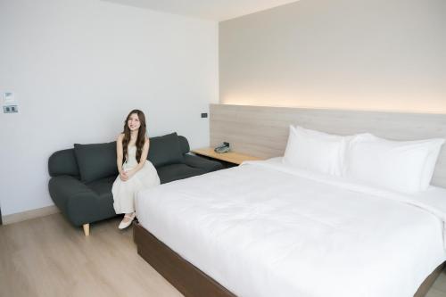 a woman sitting in a room with a bed and a couch at The Horizon Groove Hotel in Ban Khlong