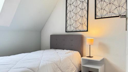 a white bedroom with a bed and a lamp at Relais du Dompeter in Molsheim