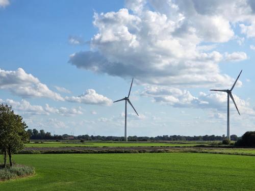 three wind turbines in a green field with a cloudy sky at Küstenkännchen in Wangerland