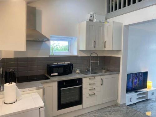 a kitchen with white cabinets and a sink and a microwave at Firdaus Loft Haven in Huddersfield in Golcar