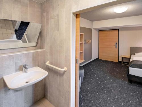 a bathroom with a sink and a room with a bed at B&B HOTEL Kassel-Industriepark in Kassel