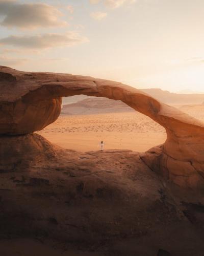 a person standing under an arch in the desert at Wadi Rum, Hala bubbles in Wadi Rum