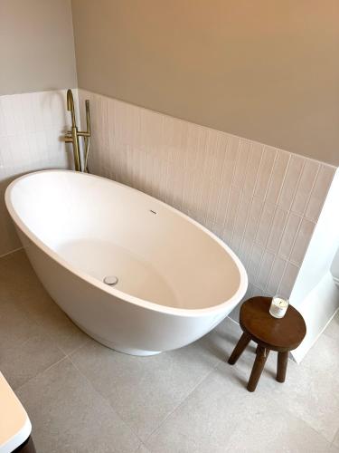 a large white tub in a bathroom with a wooden stool at Seaside retreat in Mudeford in Mudeford