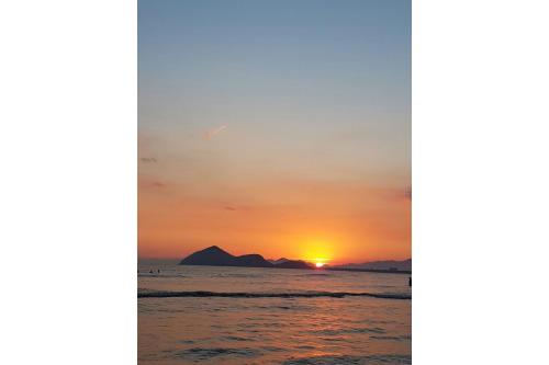a sunset on the beach with a mountain in the background at Residencial Villa Cris - Jd. São Lourenço/Itaguaré in Bertioga