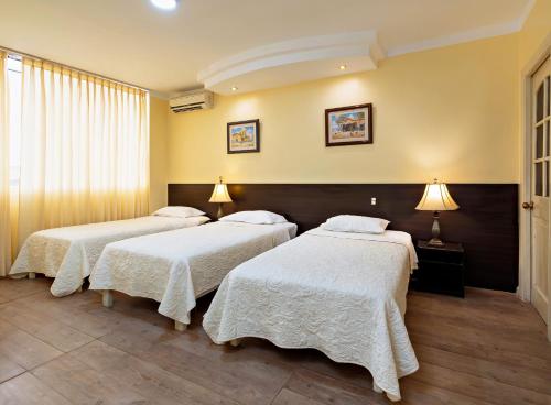 a room with three beds with white blankets at Gran Bolivar Hotel - Trujillo, Perú in Trujillo