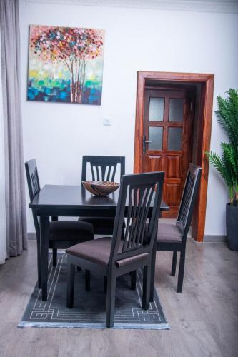 a black dining room table with four chairs and a painting at La Consolata Villa Olympia Extension in Lusaka