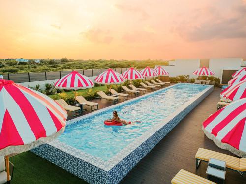 a woman in a pool with umbrellas and chairs at Privada Stays - Lofts with Private Pool and Oasis, near Eagle Beach in Palm-Eagle Beach