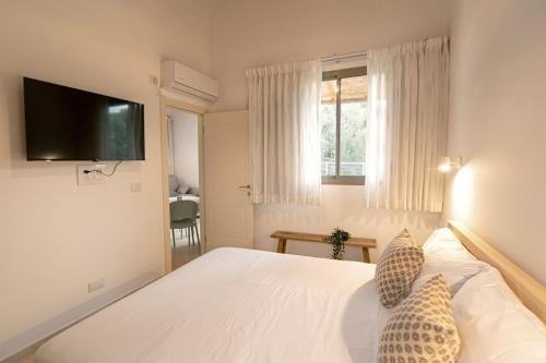 a bedroom with a white bed with a television on the wall at חווייה של שקט- מתחם שלם עם בריכה- רק בשבילכם in Livnim