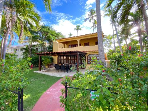 a yellow house with a patio and palm trees at SANDY BAY VILLAS and SUITES playa LOS CORALES in Punta Cana