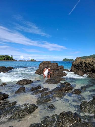 two people are standing on rocks in the ocean at La posada in Nuquí