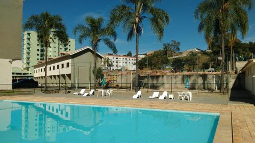 a swimming pool with white chairs and palm trees at Hotel Santiago in Lindóia