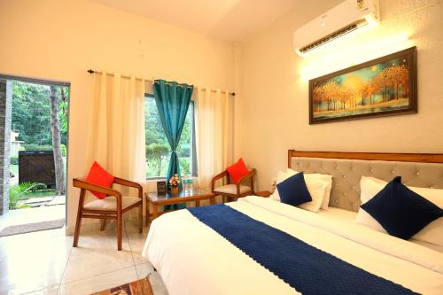 a bedroom with a bed and a table and a window at Aranya Resort & Suites By Shivaneel Hospitality in Rāmnagar