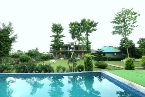 a swimming pool in front of a yard with a house at Aranya Resort & Suites By Shivaneel Hospitality in Rāmnagar