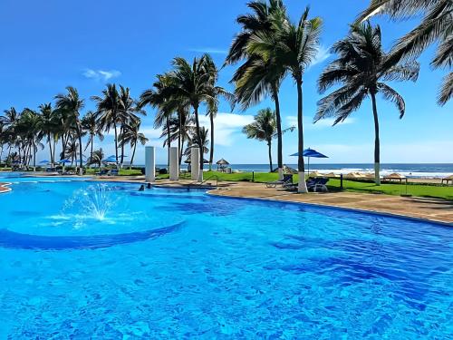 a swimming pool with palm trees and the beach at Departamento Mayan Island - A pie de playa y con albercas in Acapulco