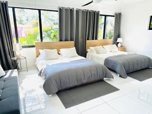 two beds in a white room with windows at Palm Breeze Getaway in Hollywood