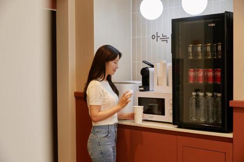 コヤンにあるAank Hotel Ilsanのカウンターに立ってコーヒーを飲む女性