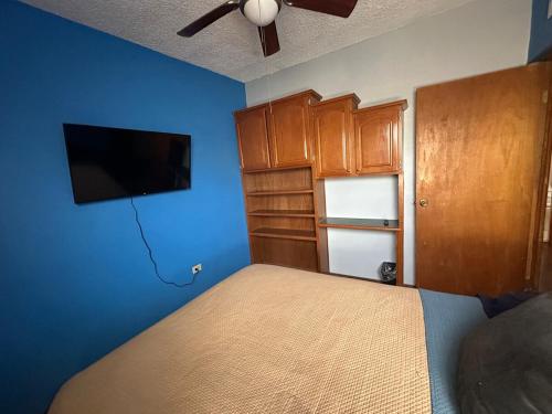 a bedroom with a bed with blue walls and a flat screen tv at Casa cerca del Consulado Americano Cs in Manuel F. Martínez