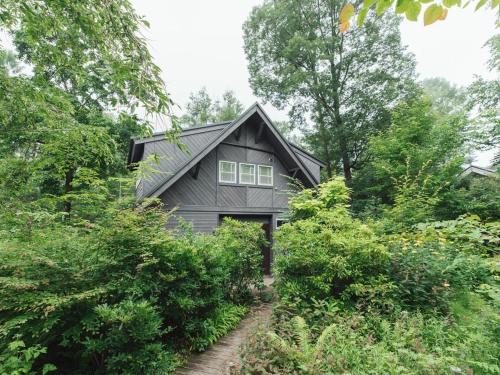 a gray house surrounded by trees and bushes at Izumigo AMBIENT Yatsugatake Cottage in Hokuto