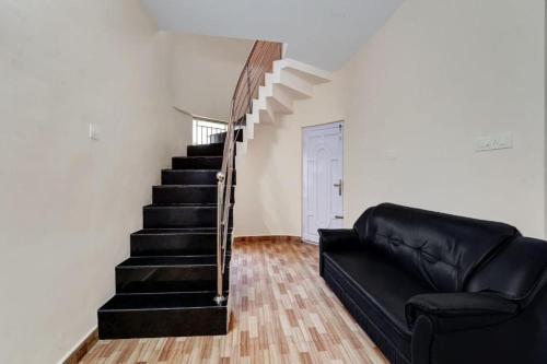 a living room with a black leather couch and stairs at Kodai Mist Starlight Hotels in Kodaikānāl