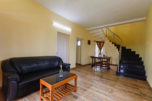 a living room with a black leather couch and stairs at Kodai Mist Starlight Hotels in Kodaikānāl