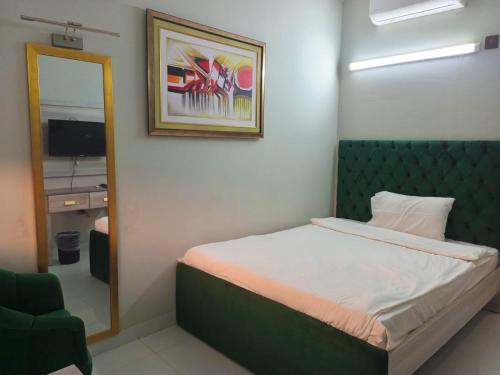 a bedroom with a bed with a green headboard and a mirror at Airport Hotel in Karachi