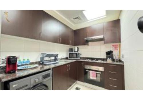 a kitchen with brown cabinets and a stove top oven at 1BR Urban Oasis - Chic Poolside Retreat in Abu Dhabi