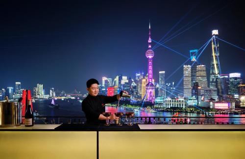 a man standing at a bar with a view of a city at The Peninsula Shanghai in Shanghai