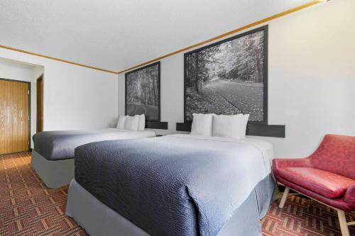 two beds in a hotel room with a red chair at Super 8 by Wyndham Eveleth in Eveleth