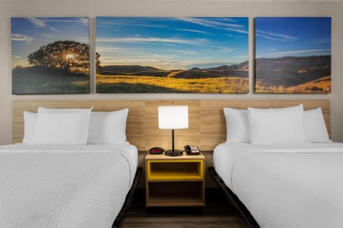 two beds in a room with three paintings on the wall at Days Inn and Suites by Wyndham Hammond, IN in Hammond