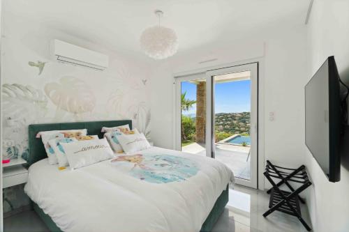 a white bedroom with a bed and a large window at Villa L'Emeraude in Cavalaire-sur-Mer