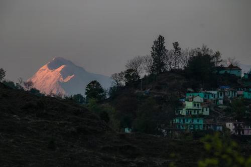a mountain in the distance with houses on a hill at Himkosi Farm by the River in Almora