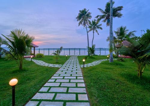 a stone path leading to the beach with palm trees at Ashtamudi Luxe Villa by VOYE HOMES in Kollam