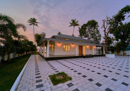 a small house on a tiled courtyard with trees at Ashtamudi Luxe Villa by VOYE HOMES in Kollam