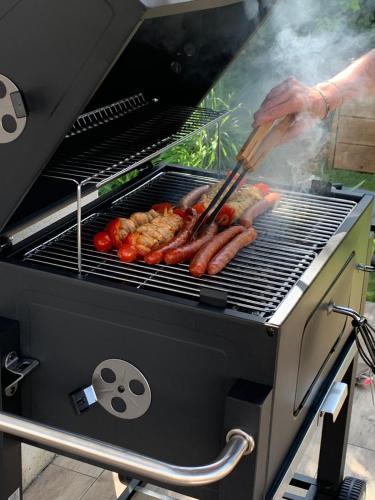 a person cooking hot dogs and sausages on a grill at Villa Meyzieu Grand Large in Meyzieu