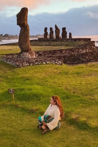 a woman sitting on the grass in front of a statue at Mai 'Uta Experience in Hanga Roa