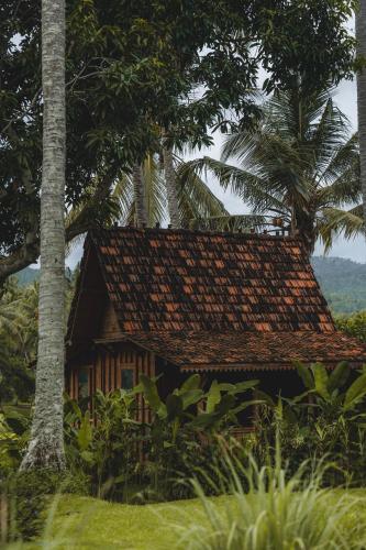 a house with a thatched roof and palm trees at Desa Cabins in Balian