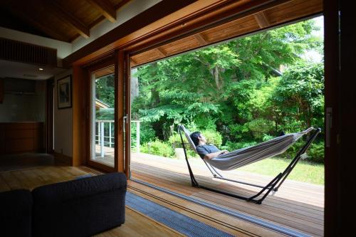 a man sitting in a hammock on a porch at 箱根こもれび庵 in Hakone