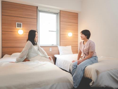 two women sitting on beds in a hotel room at Super Hotel Premier Shimonoseki in Shimonoseki