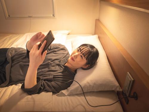 a man laying on a bed holding a remote control at Super Hotel Premier Shimonoseki in Shimonoseki