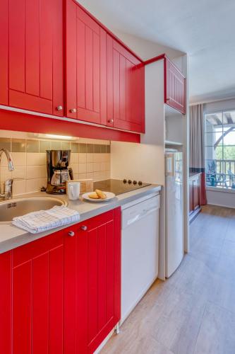 a kitchen with red cabinets and a white dishwasher at Résidence Pierre & Vacances Le Domaine de Gascogne in Biscarrosse