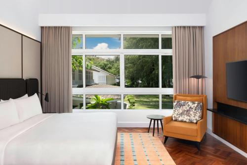 a bedroom with a bed and a chair and a large window at Lone Pine, Penang, a Tribute Portfolio Resort in Batu Ferringhi