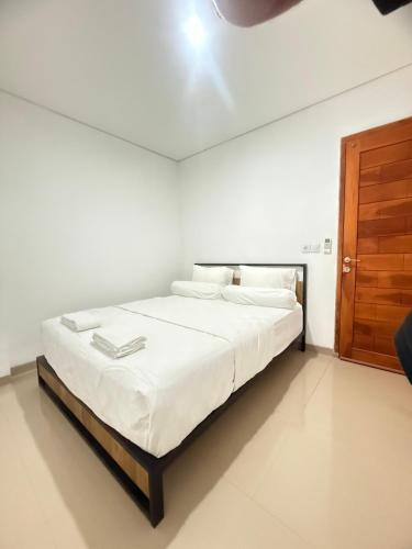 a bedroom with a bed with white sheets and a wooden door at Home Stay Room in Bali Near Sanur Beach in Sanur